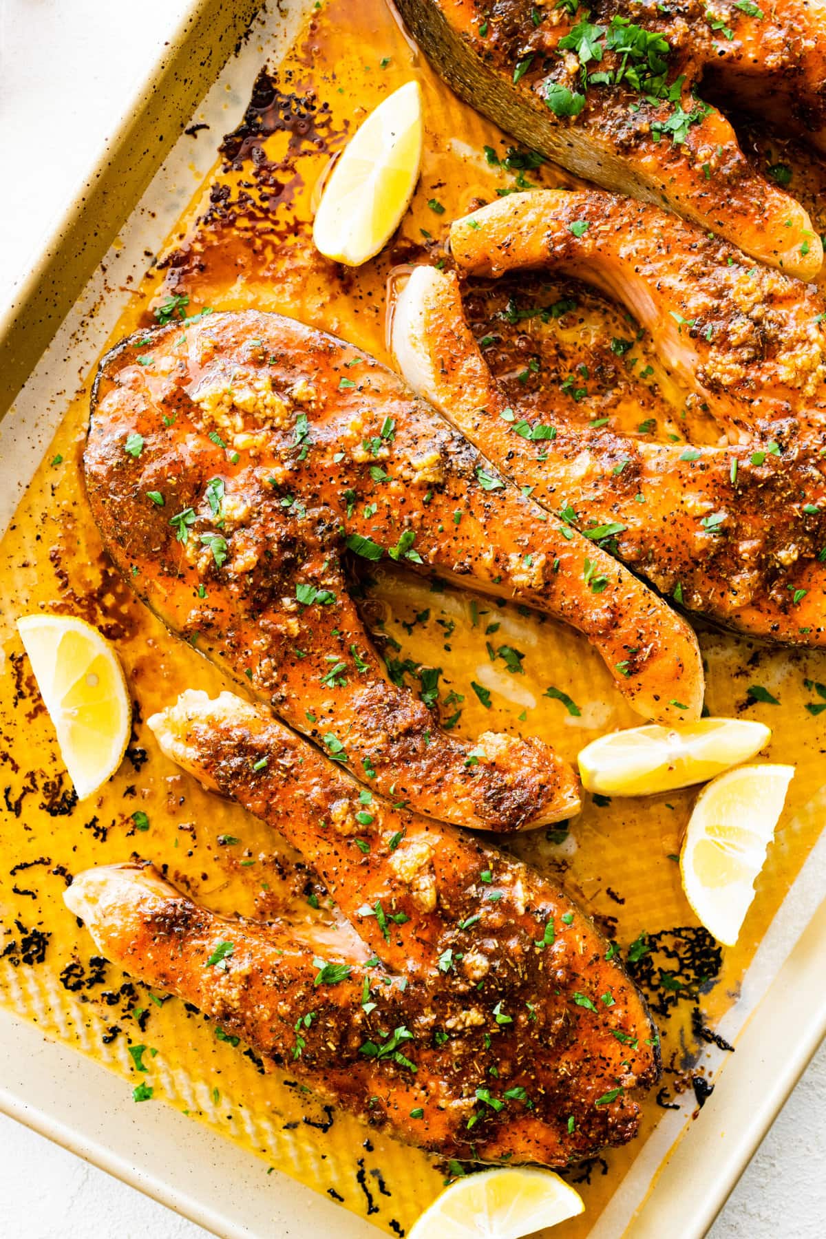 baked salmon steaks on a baking sheet with a nice sear on the top. Lemon slices on the tray.