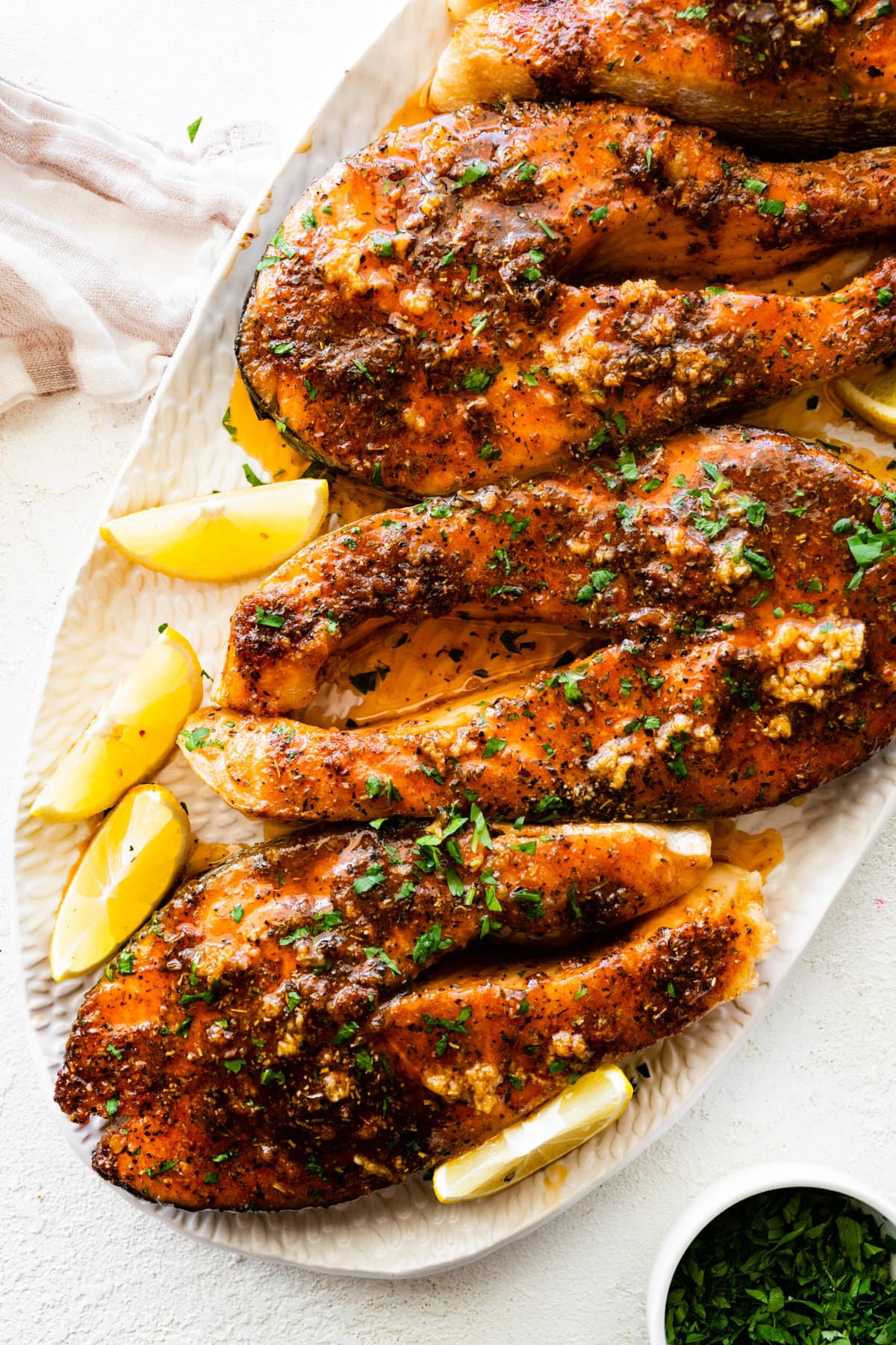 salmon steaks on a white serving platter with lemon slices on the side.