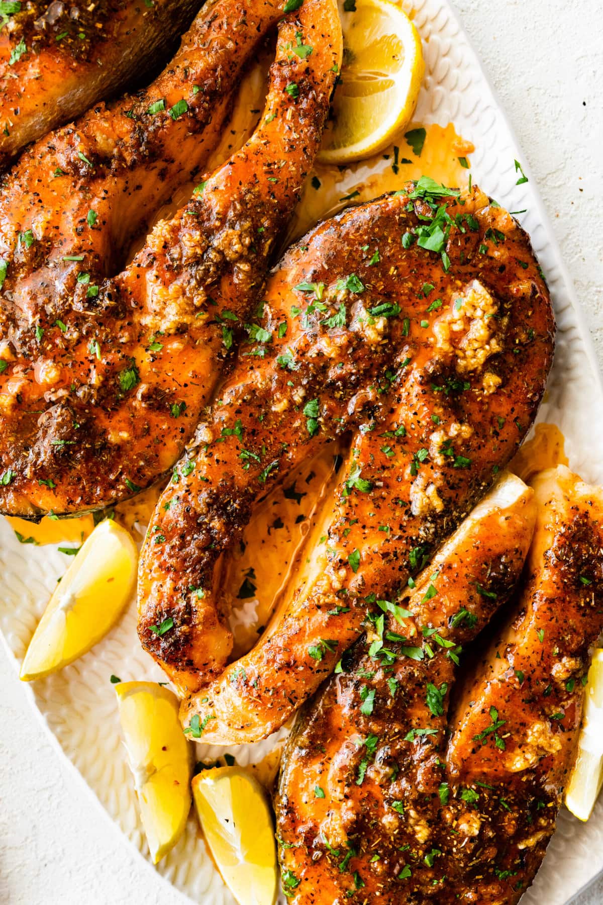 salmon steaks on a white serving platter with lemon slices on the side.