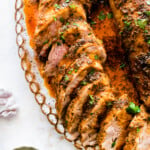 perfectly cooked pork tenderloin in baking pan with juices. Parsley on the side.