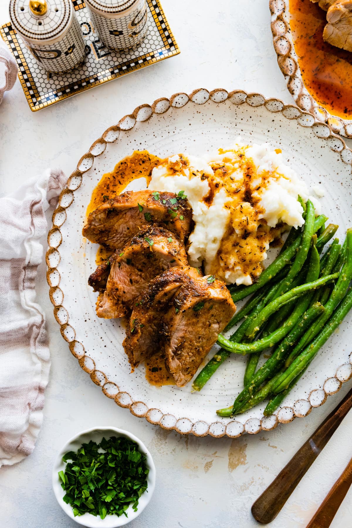 pork tenderloin slices on a plate with green beans and mashed potatoes. pan juices over the top.