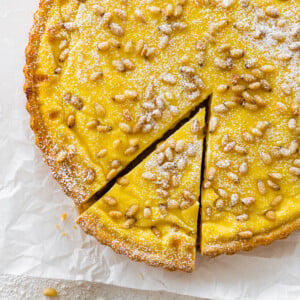 finished torta della nonna with pine nuts on top after baking. a light dusting of powdered sugar. One slice taken out of the torta. cover photo.