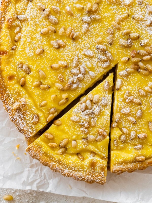 finished torta della nonna with pine nuts on top after baking. a light dusting of powdered sugar. One slice taken out of the torta. cover photo.