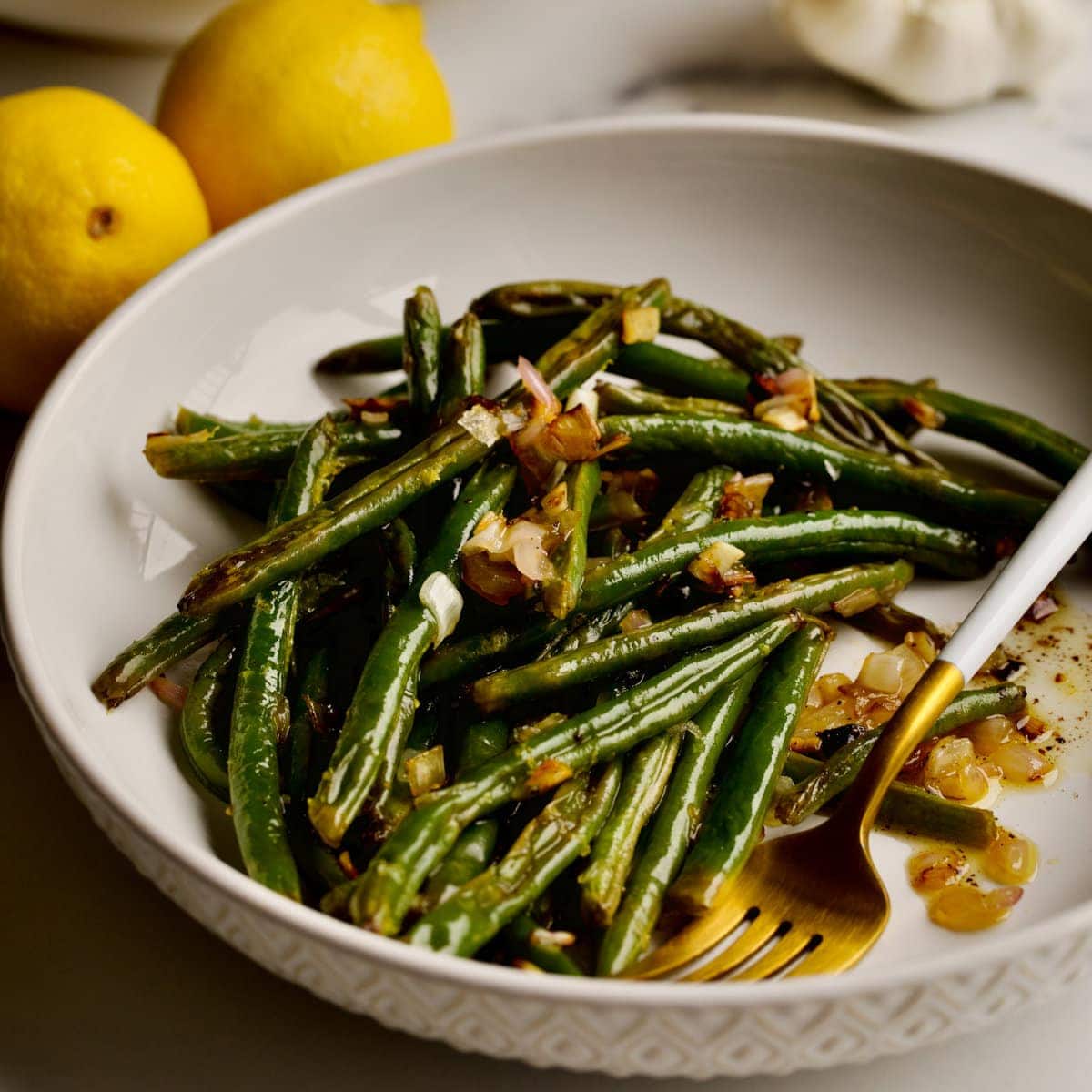 green beans in a white bowl with a gold fork