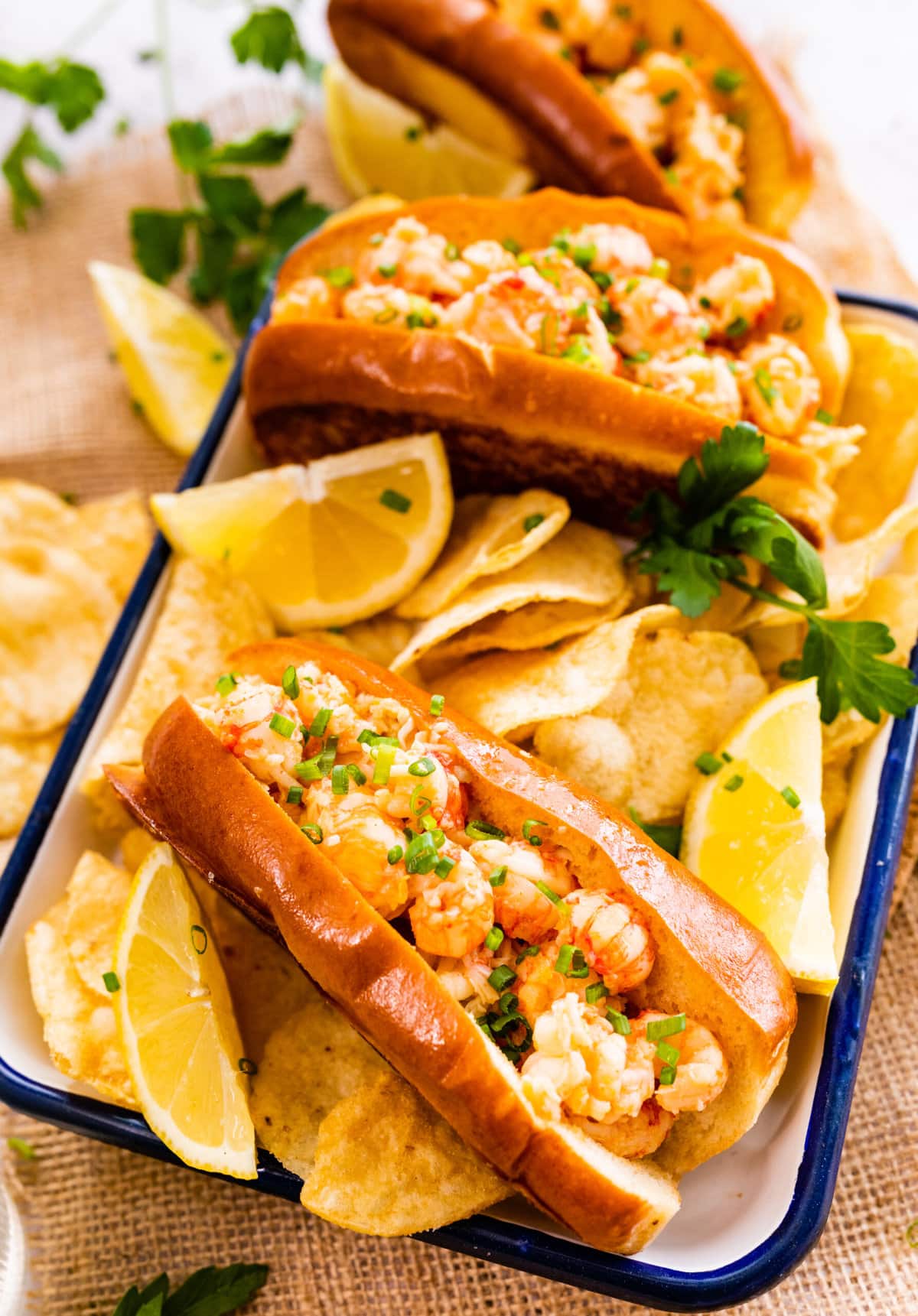 assembled sandwiches in a white and blue tray with chips and lemon wedges on the side.