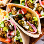 plate of falafel pitas with all the condiments in the pita. Plus a bowl of hummus and extra sauce. and pickled red onions.