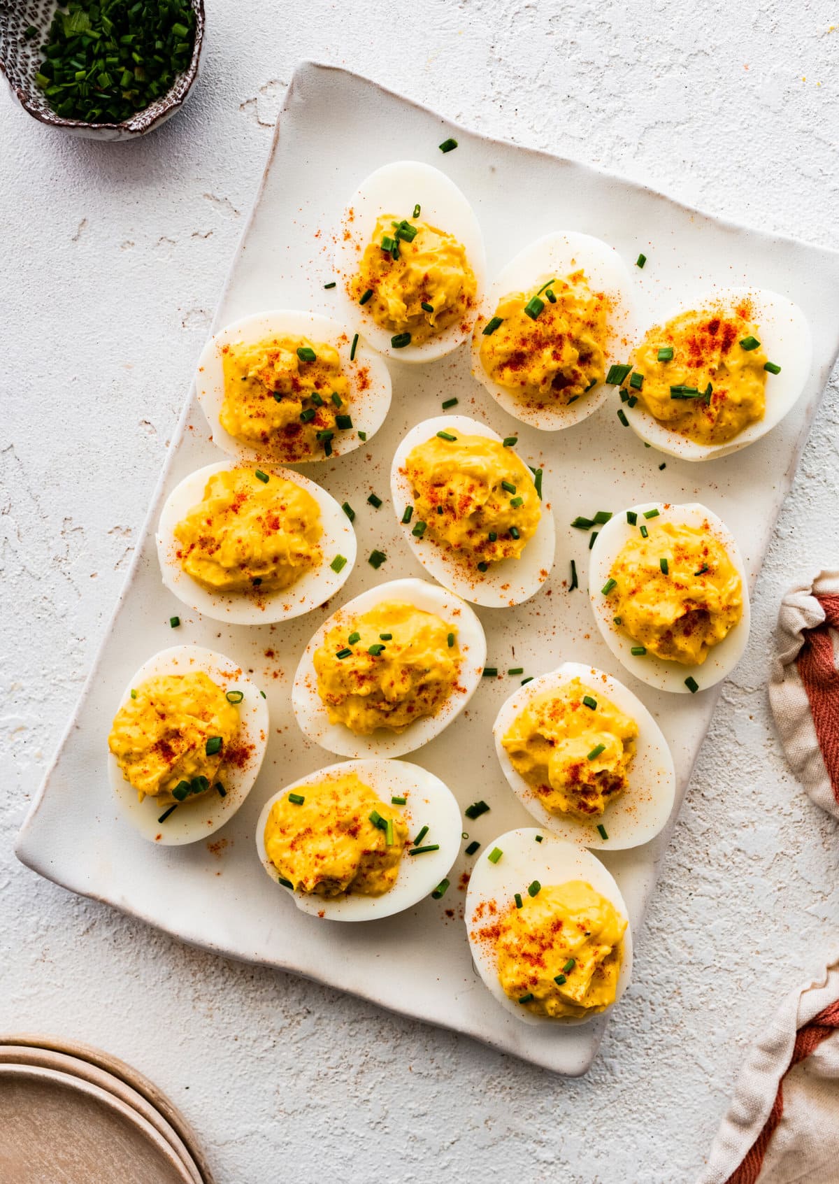 plate of deviled egg with paprika on top arranged on a plate with a few chives on top.