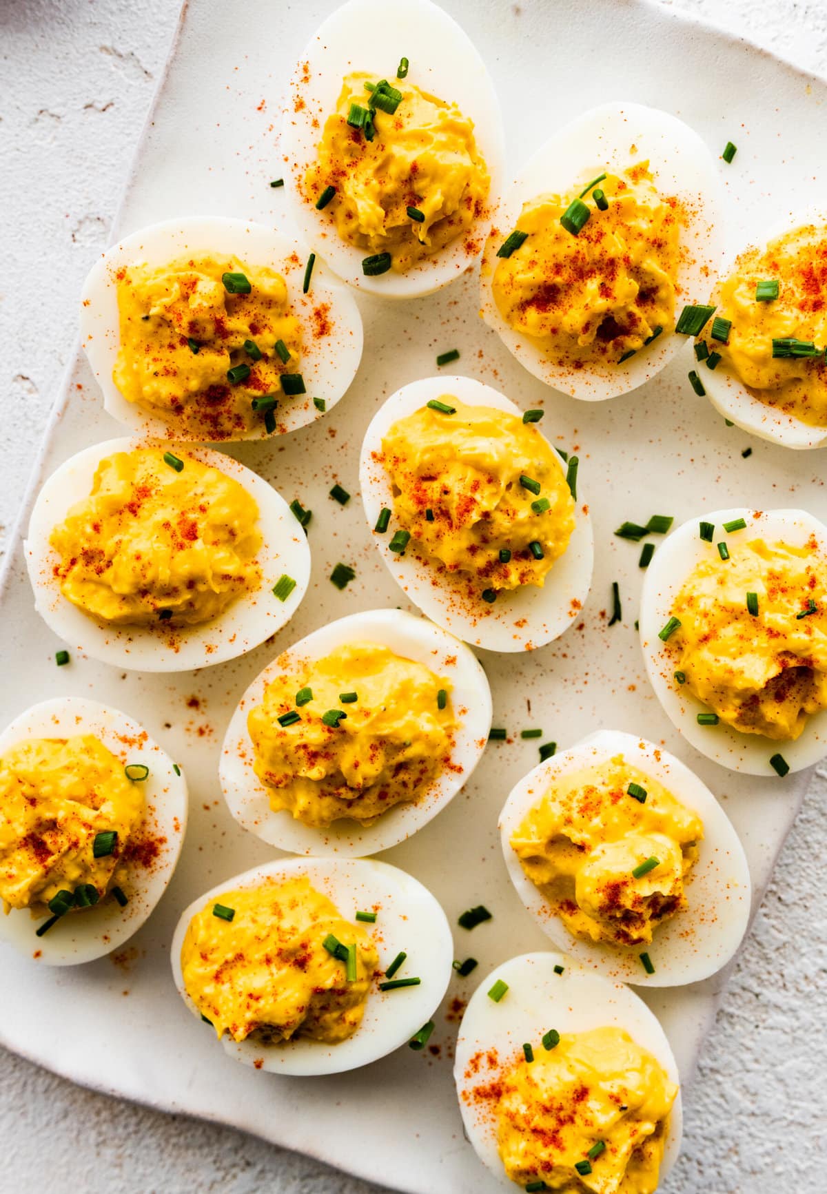 plate of deviled egg with paprika on top arranged on a plate with a few chives on top.