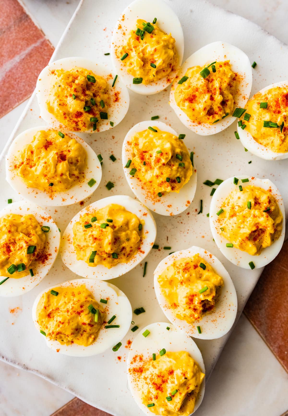plate of deviled egg with paprika on top arranged on a plate with a few chives on top. 