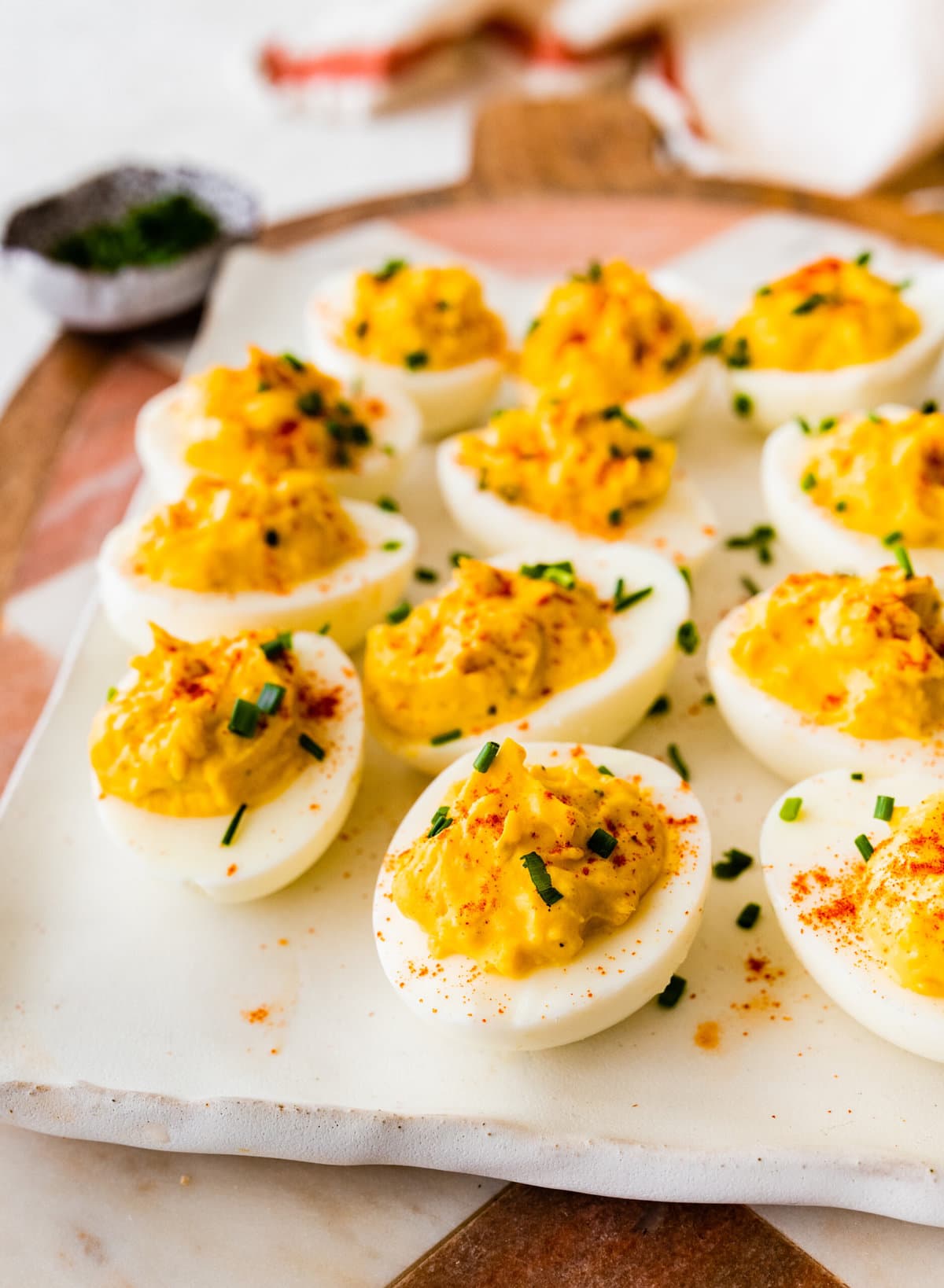 plate of deviled egg with paprika on top arranged on a plate with a few chives on top.