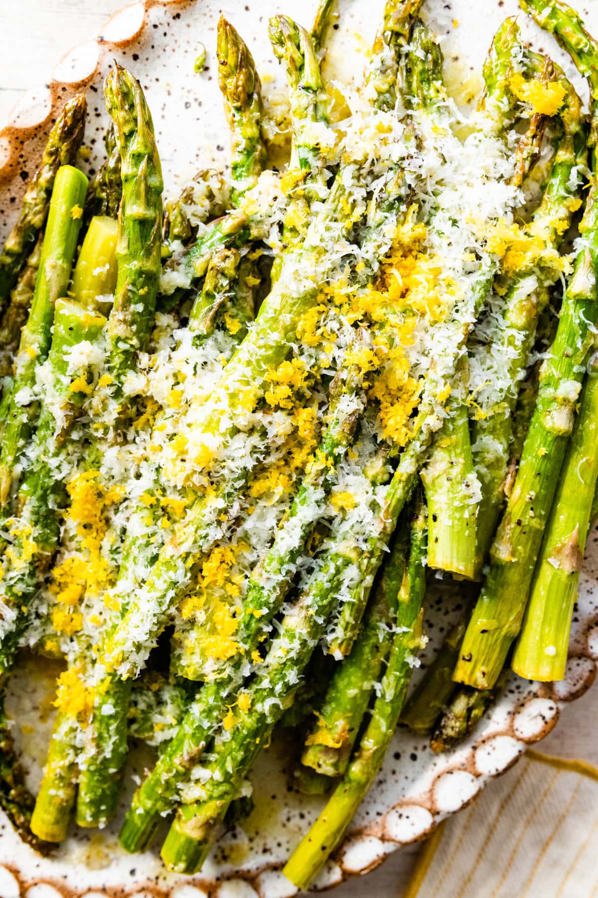 asparagus finished cooking on a white platter with freshly grated parmigiano and lemon on it.