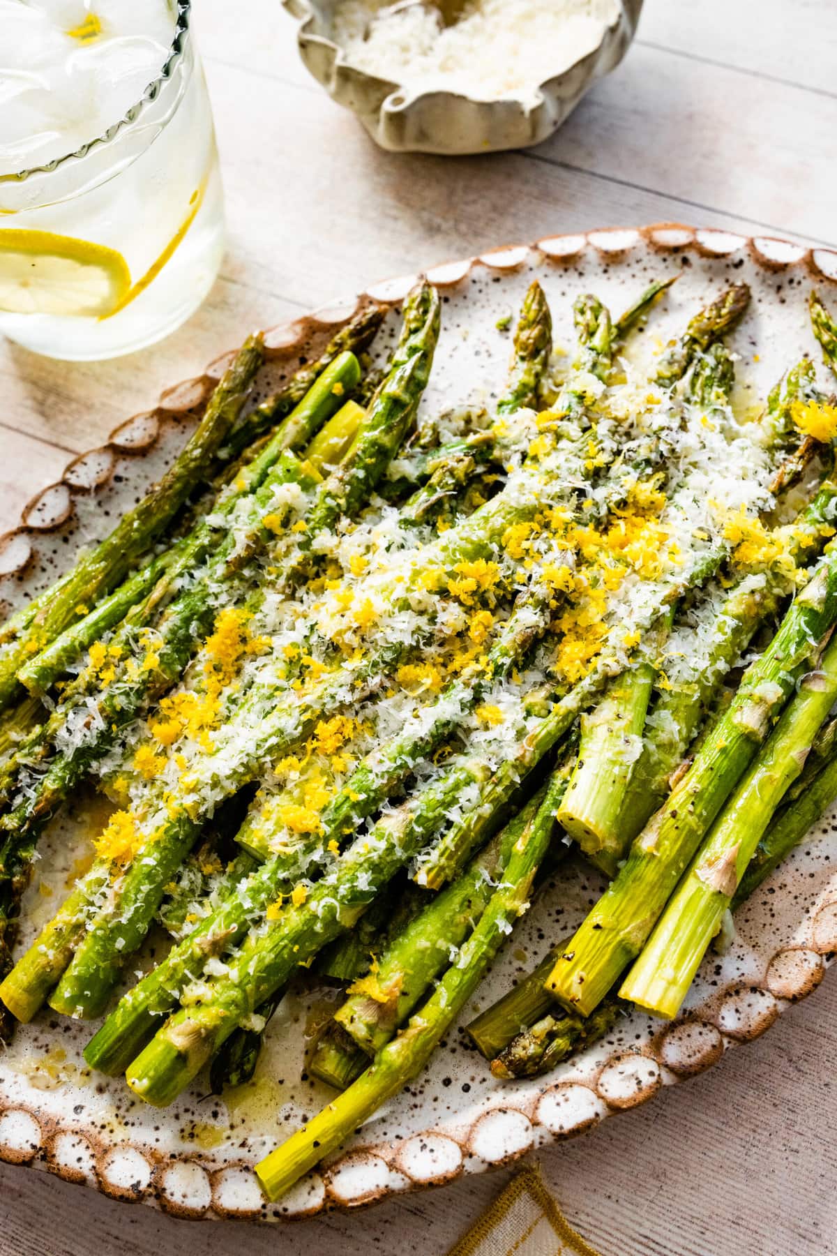 asparagus finished cooking on a white platter with freshly grated parmigiano and lemon on it. 