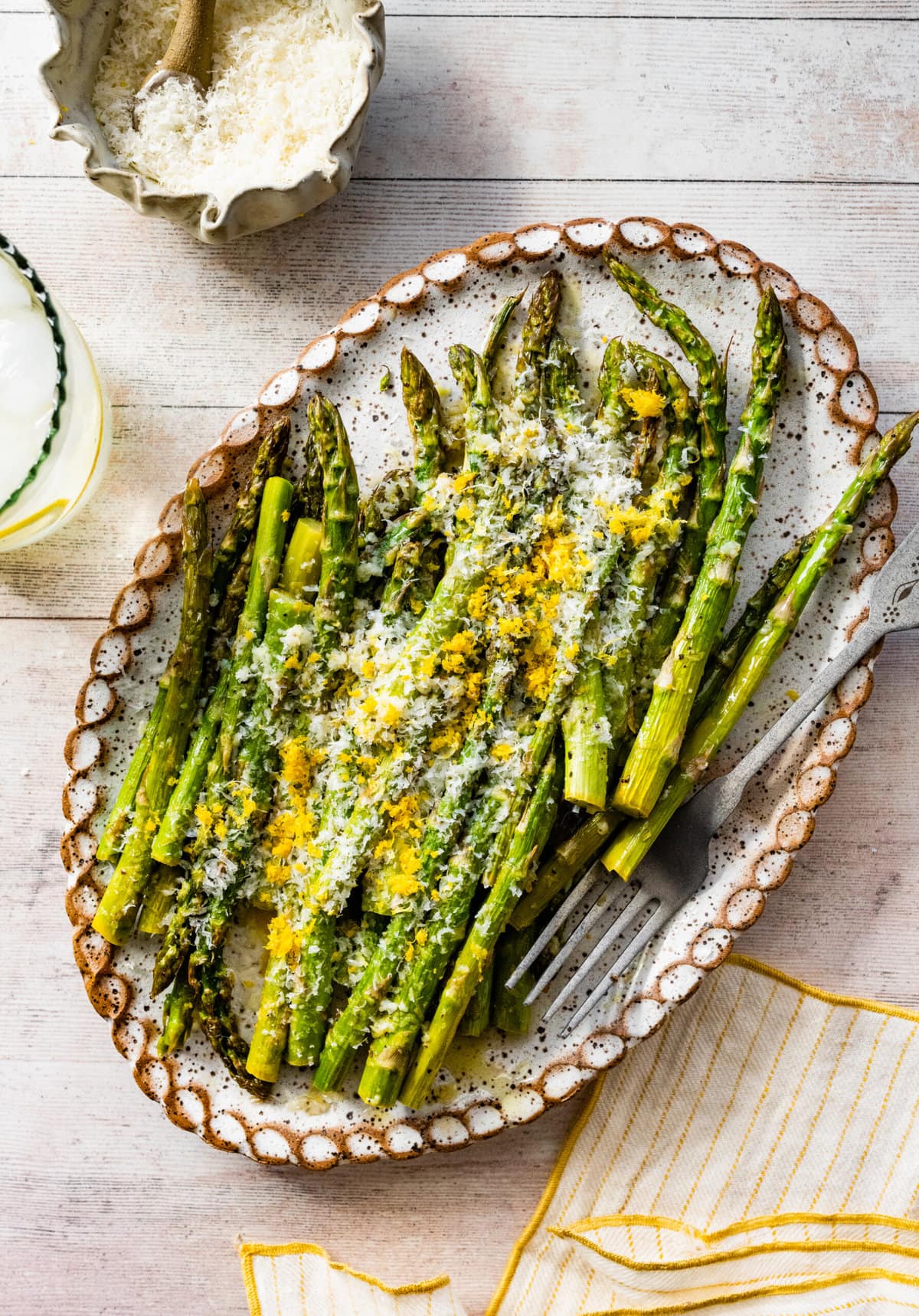 asparagus finished cooking on a white platter with freshly grated parmigiano and lemon on it.