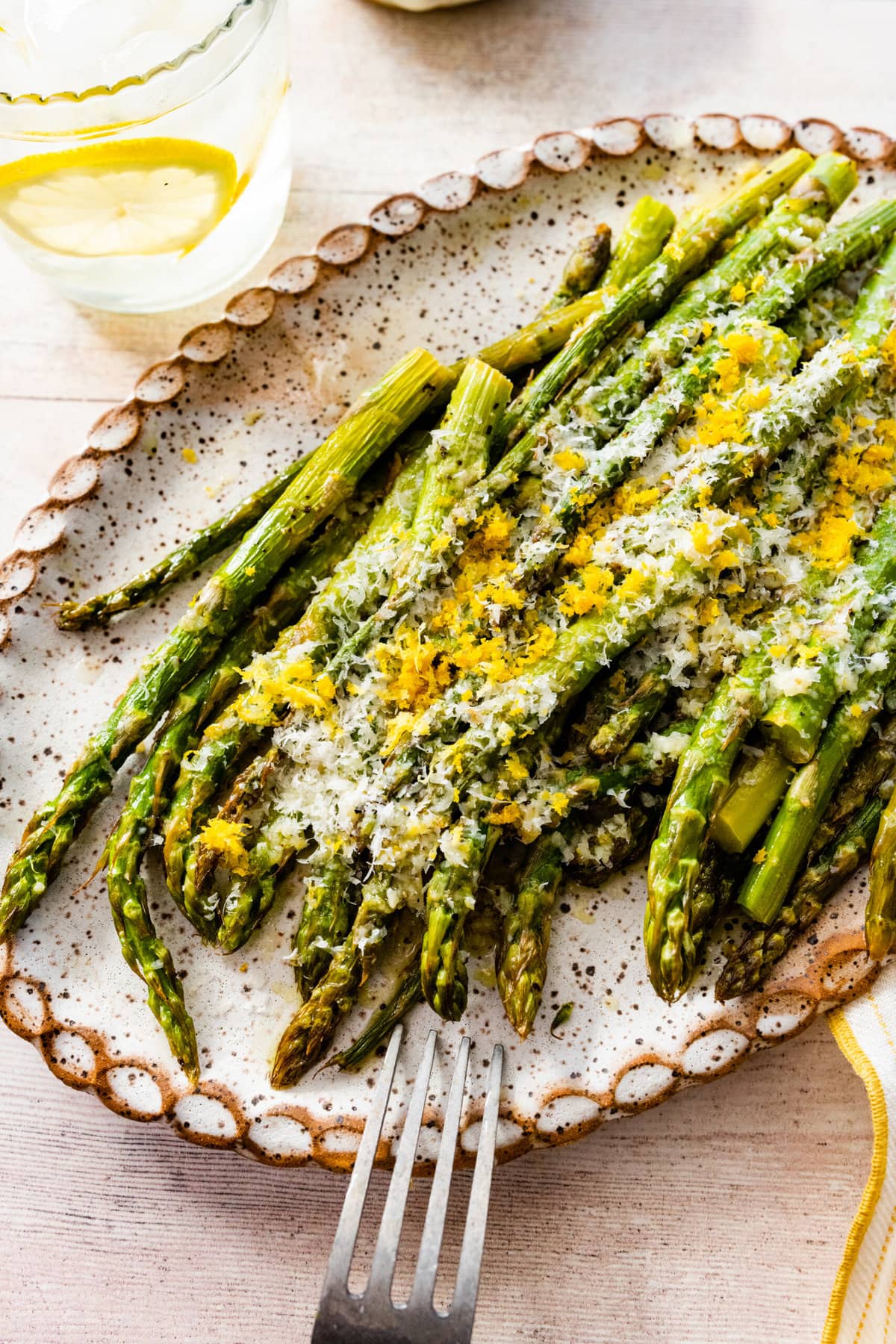asparagus finished cooking on a white platter with freshly grated parmigiano and lemon on it. Fork on plate.