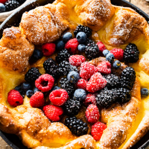 Dutch baby pancake topped with powdered sugar and berries in a cast iron skillet.