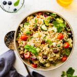 finished greek orzo pasta salad recipe in a large serving bowl with ingredients around it.
