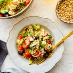greek salad in a bowl with a fork. Big orzo greek salad bowl in the background.