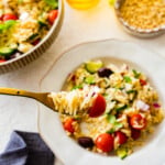 greek salad in a bowl with a fork. Big orzo greek salad bowl in the background. Bite on a fork.