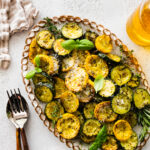 Easy Oven Roasted Zucchini and Yellow Squash Recipe on a platter with basil on the top. Parmigiano cheese on the side. Serving utensils on the side.