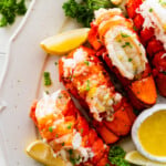 steamed lobster tails on a white plate, curly parsley, and lemon.