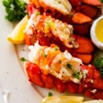 steamed lobster tails on a white plate, curly parsley, and lemon.