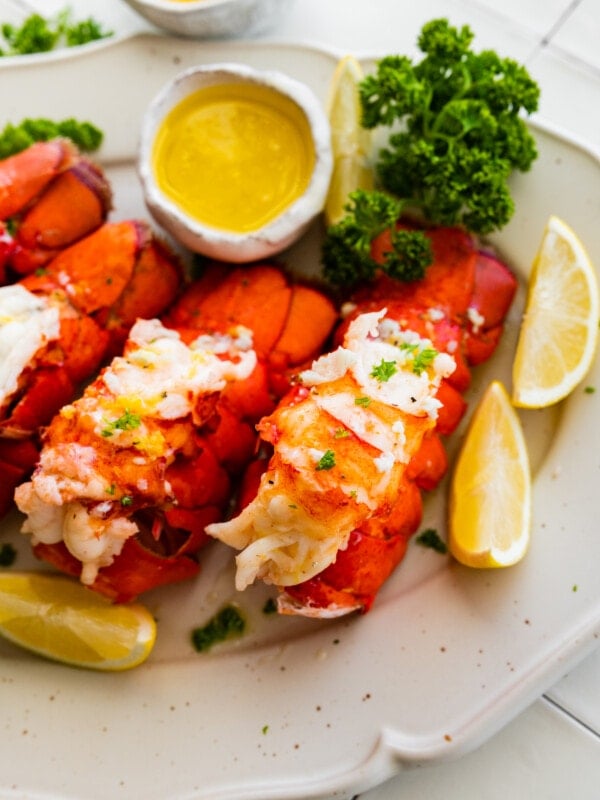 Steamed lobster tails on a plate with garlic butter and lemon wedges.