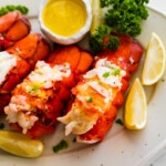 steamed lobster tails on a white plate, curly parsley, and lemon.