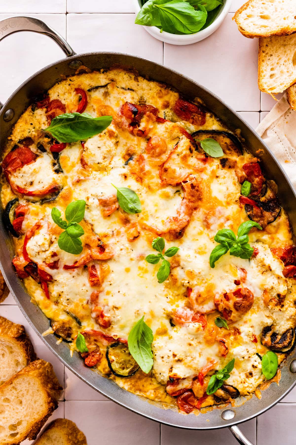 Layered Eggplant, Zucchini, Tomato Casserole with bubbly cheese and basil leaves to garnish.
