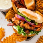 Ultimate grilled chicken sandwiches on a tray with parchment paper. Waffle fries and aioli on the side.