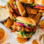 Ultimate grilled chicken sandwiches on a tray with parchment paper. Waffle fries and aioli on the side.
