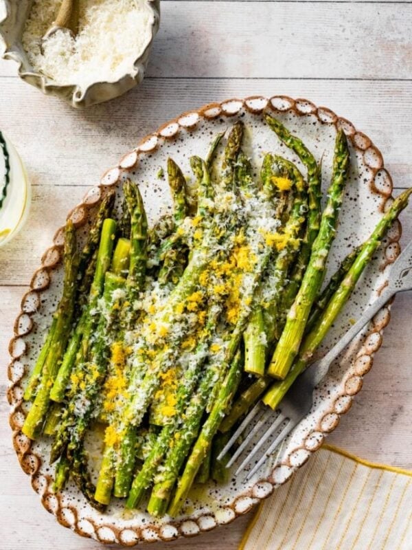 asparagus finished cooking on a white platter with freshly grated parmigiano and lemon on it.