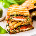 Stack of two halves of Caprese sandwich with basil pesto on parchment paper.