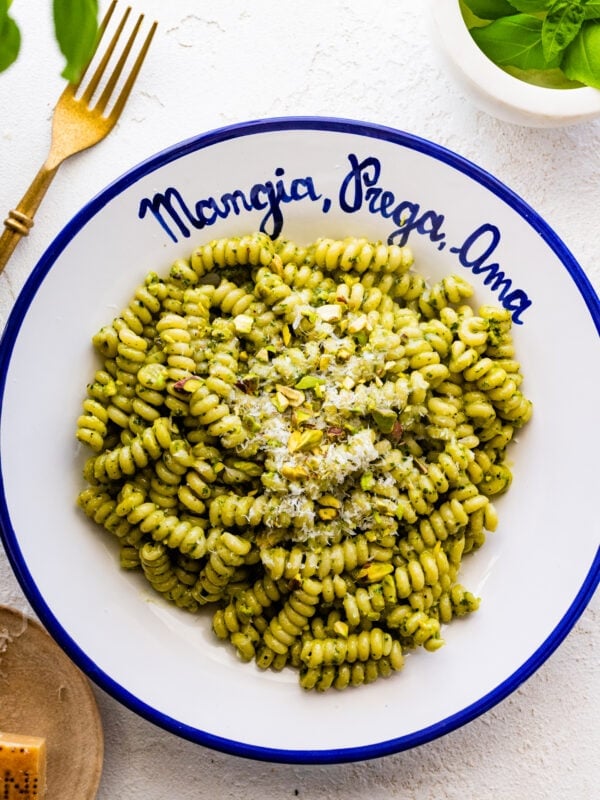platted bowl of pasta with cheese. The bowl is white and in blue is written the Italian phrase- "Mangia, Prega, Ama".