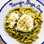 platted bowl of pasta with burrata cheese crushed pistachios on the top. The bowl is white and in blue is written the Italian phrase- "Mangia, Prega, Ama".