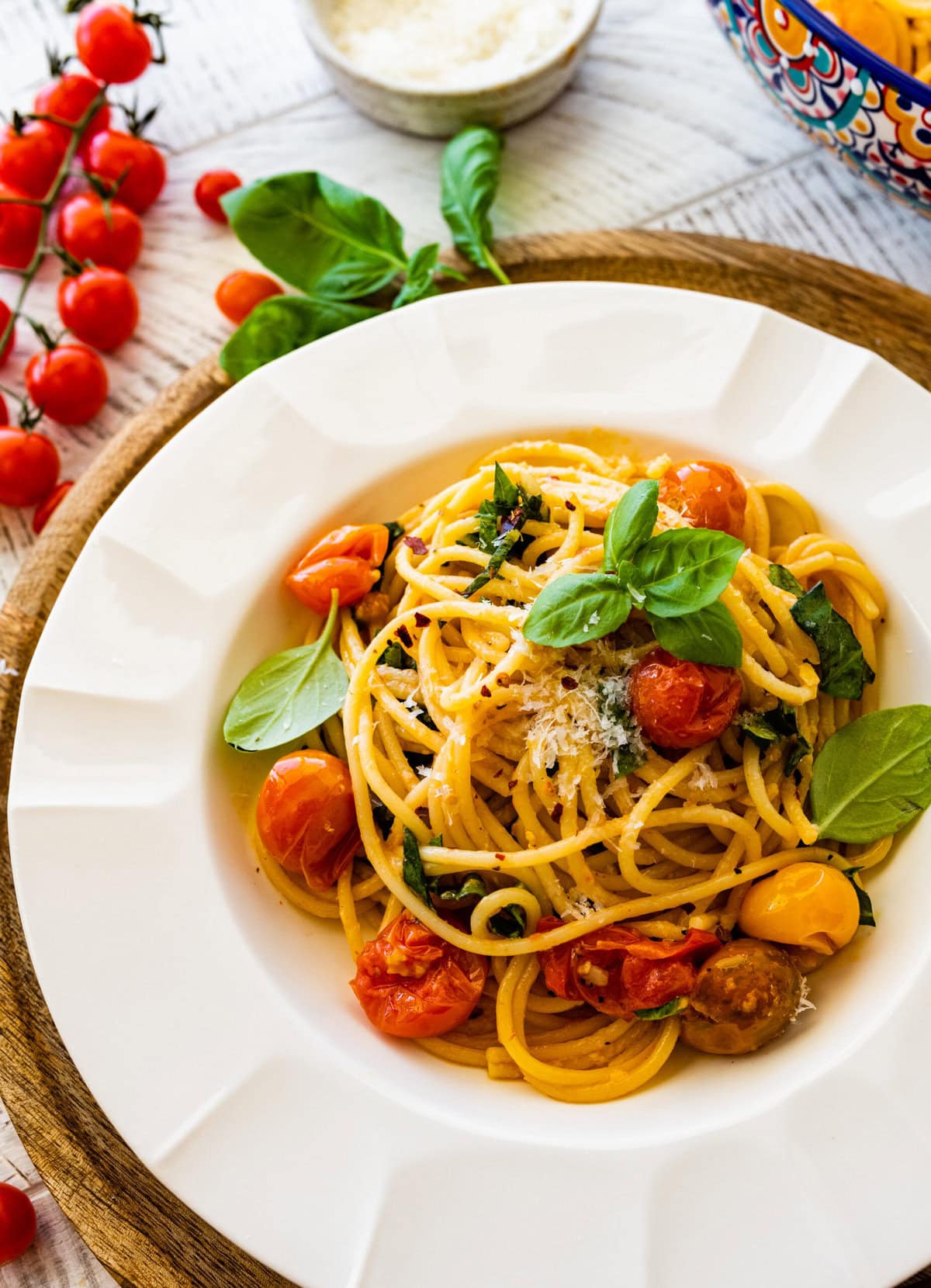 platted burst cherry tomato pasta recipe in a white bowl with basil leaves on top.