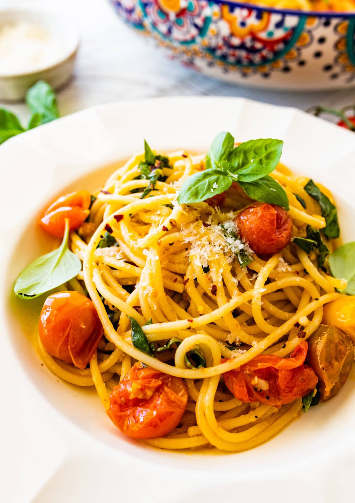 platted burst cherry tomato pasta recipe in a white bowl with basil leaves on top.
