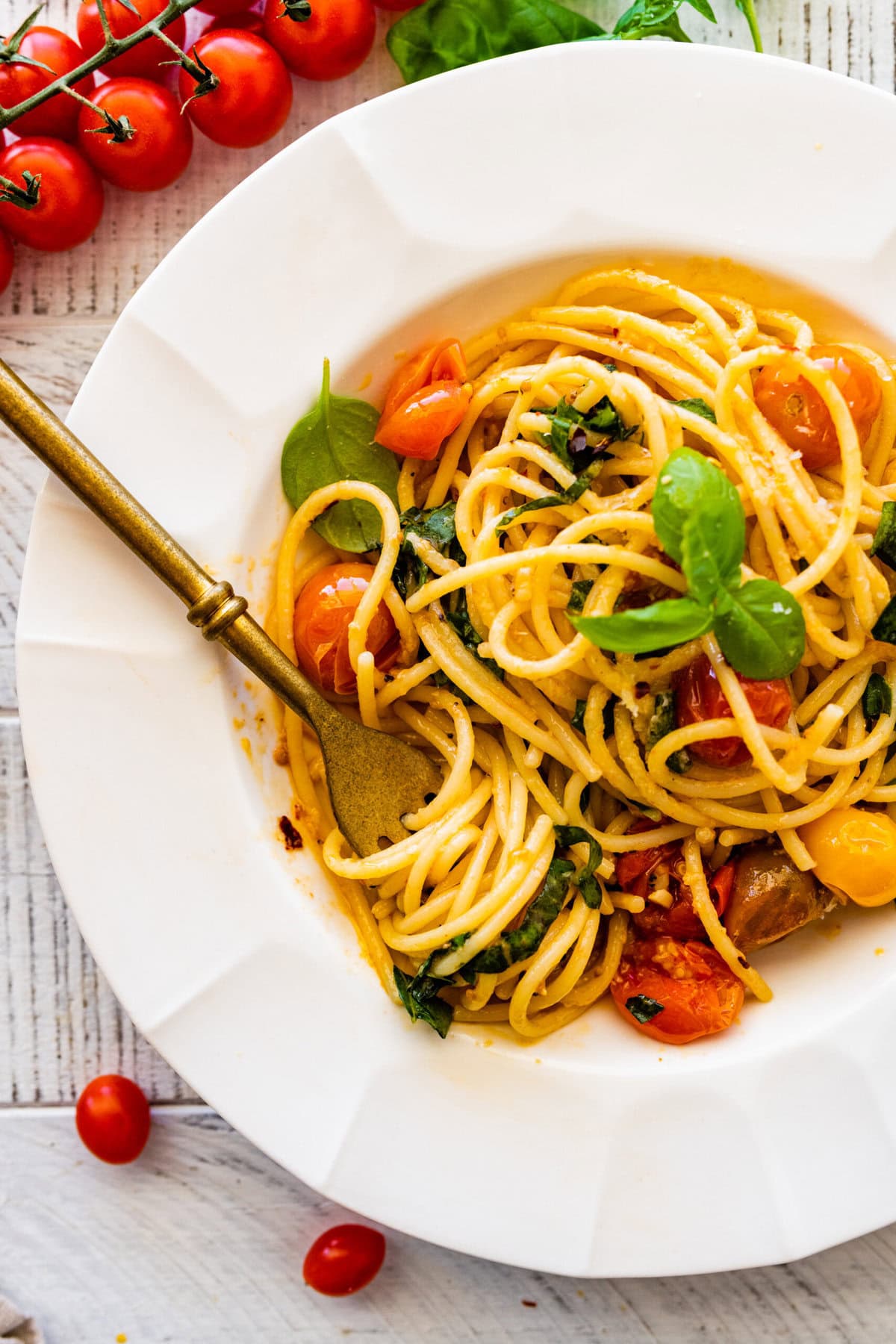 platted burst cherry tomato pasta recipe in a white bowl with basil leaves on top. Fork in the bowl ready to eat.