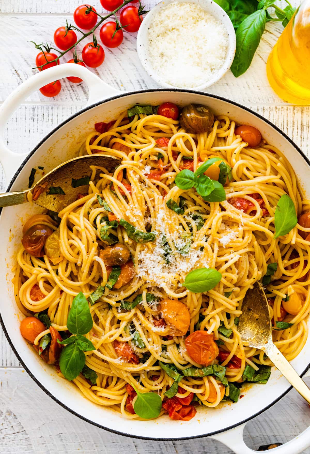 Spoons tossing pasta and cheery tomatoes in a pan.