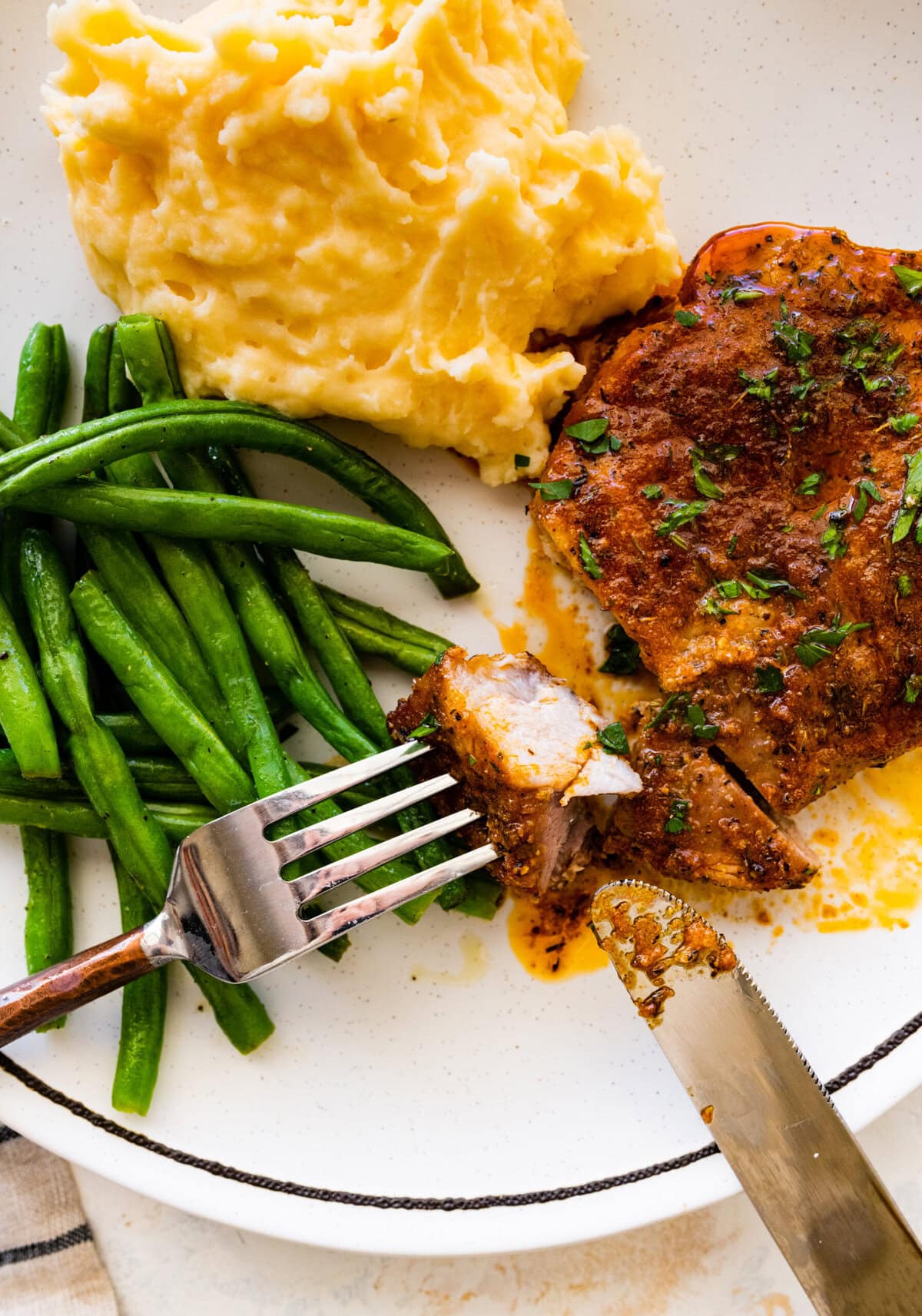 baked pork chops on a plate with green beans and mashed potatoes. bite with a fork.