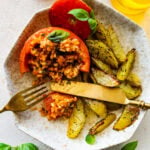 one tomato on a plate with the baked potatoes. Fork cutting into the tomato and rice to take a bite.