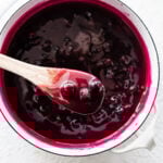 Wooden spoon with a scoop of homemade blueberry sauce from a saucepan.
