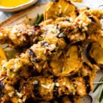 chicken spiedini recipe on a platter with grilled lemons and herbs ready to serve with dipping sauce on the top and dripping off the sides.