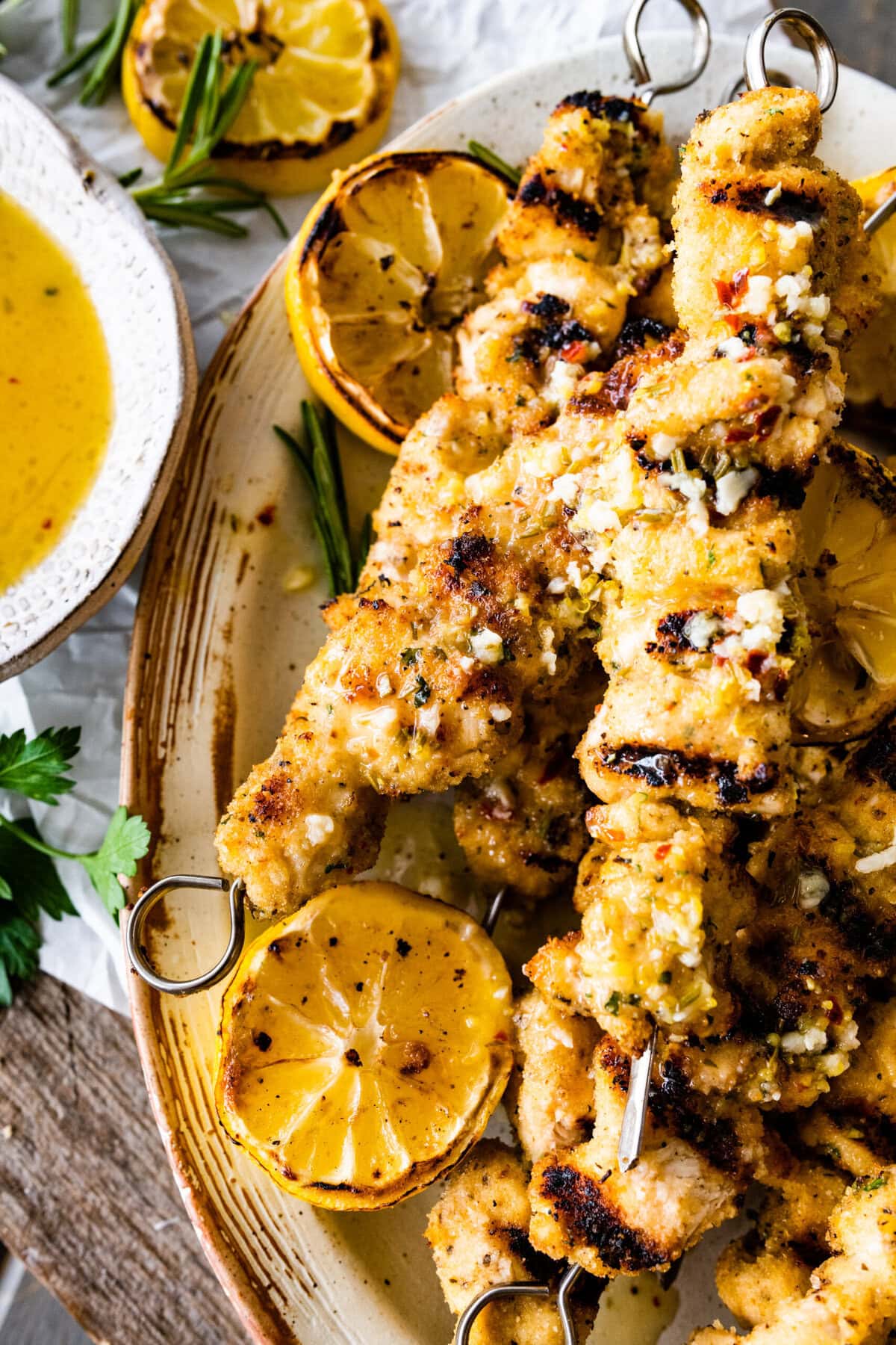 chicken spiedini recipe on a platter with grilled lemons and herbs ready to serve with dipping sauce on the top and dripping off the sides.