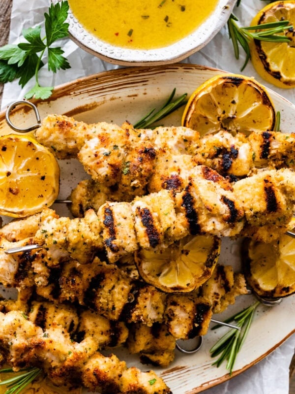 chicken spiedini recipe on a platter with grilled lemons and herbs ready to serve with dipping sauce on the top and dripping off the sides.