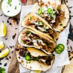 chipotle carnitas tacos on a platter with jalapenos and cream on top.