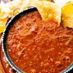 Chipotle Hot Salsa Recipe (Copycat) in a Mexican- style bowl with limes around the bowl. Chips around it and dried chilis.