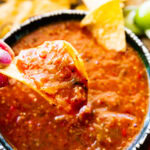 Hand holding a chip dipped in copycat Chipotle hot salsa over a bowl.