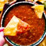 Hand holding a chip dipped in copycat Chipotle hot salsa.
