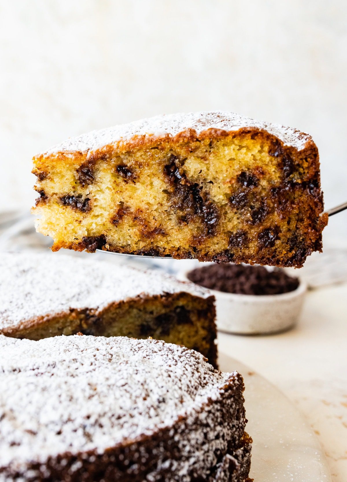 cake server holding a thick slice of the chocolate chip ricotta cake. The chocolate chips are visible. 