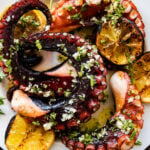 plated easy grilled octopus recipe perfectly grilled on a plate with grilled lemons and dressing. The octopus is slightly charred.